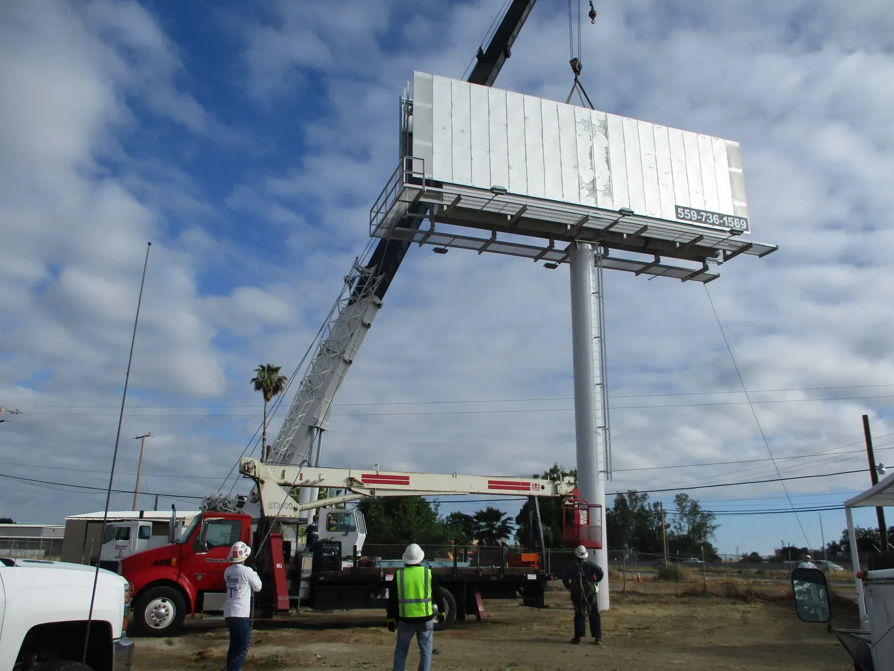 Construction crew guiding a billboard face into place with a crane