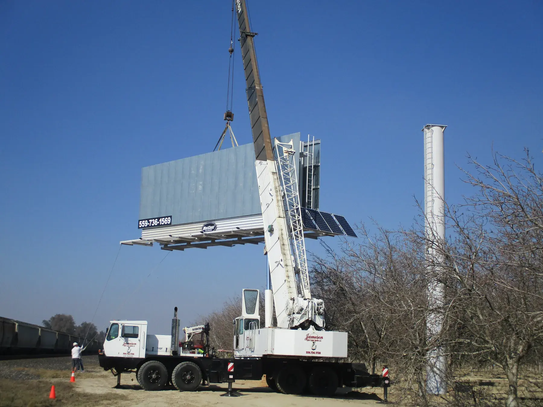 Crane positioning a billboard face near an orchard