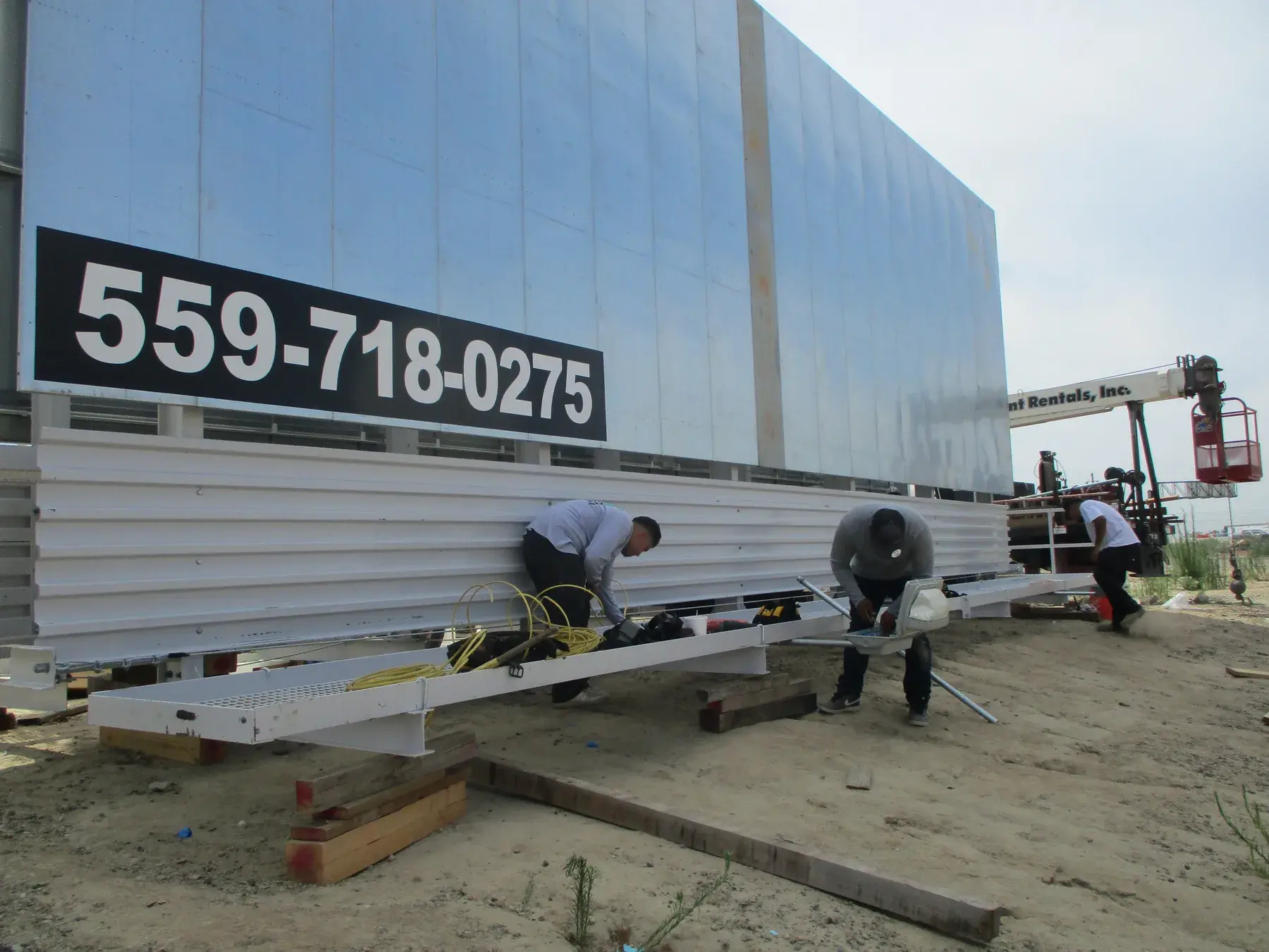 Workers completing details on a billboard structure at ground level